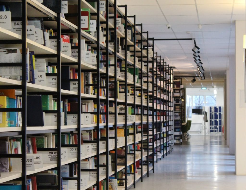 stack-of-books-in-shelf-256559 A spacious modern library with organized bookshelves and a well-lit aisle, perfect for reading and research.